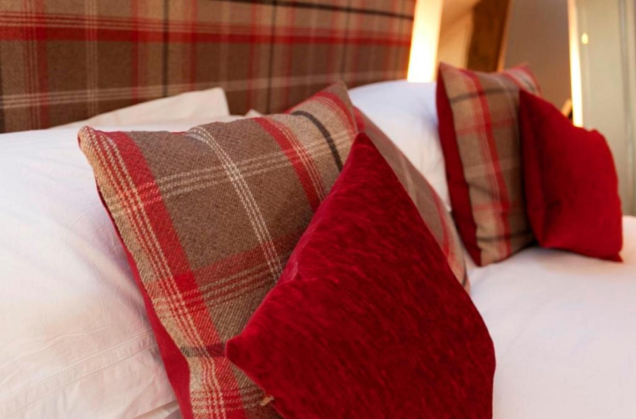 A bed with plaid and red pillows, a white bedspread, and a plaid headboard.