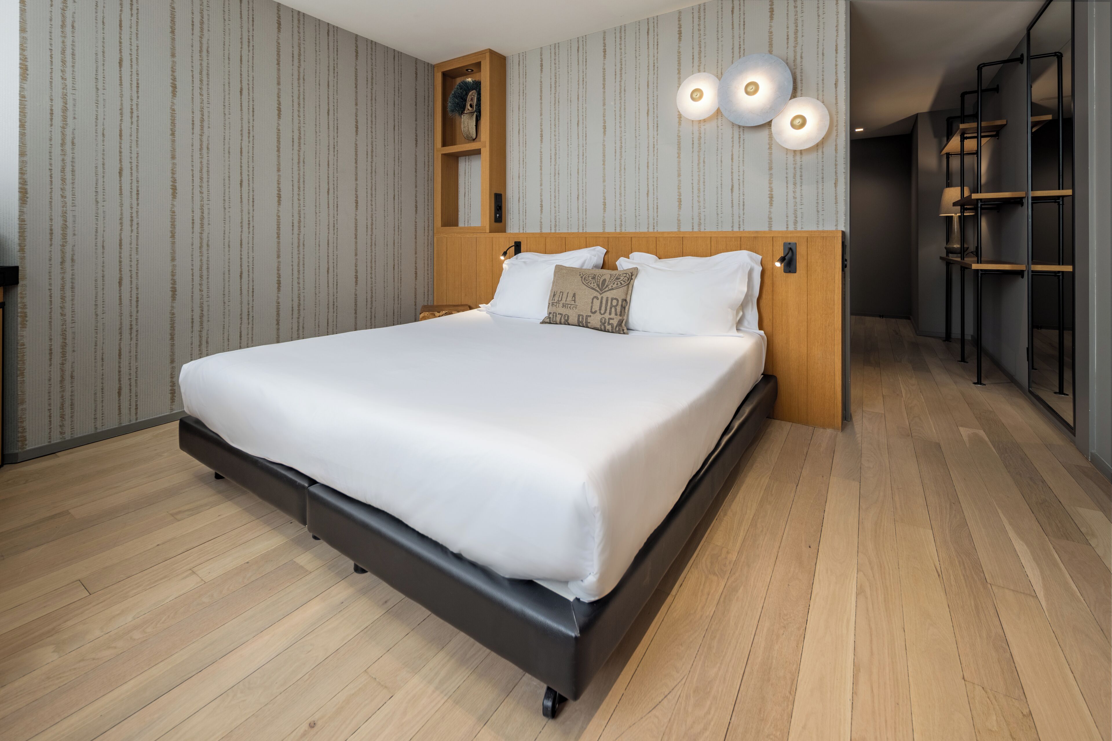 A modern bedroom with a large bed, wooden headboard, and built-in shelving.