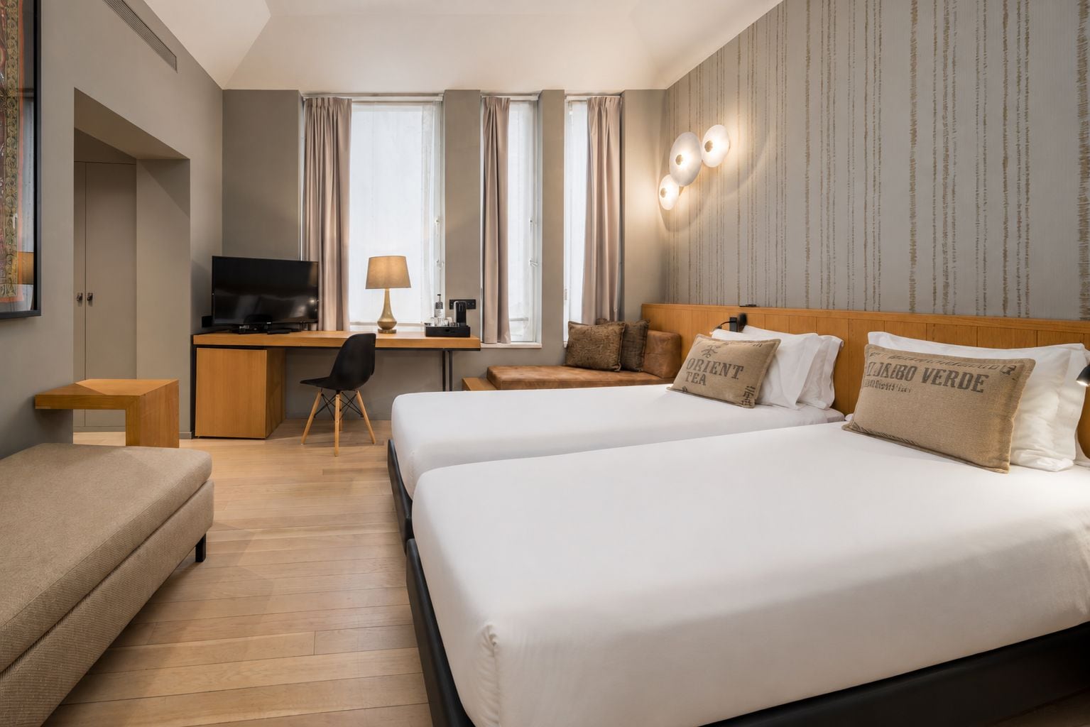 Habitación de hotel con dos camas, un escritorio, televisor y una ventana con cortinas.