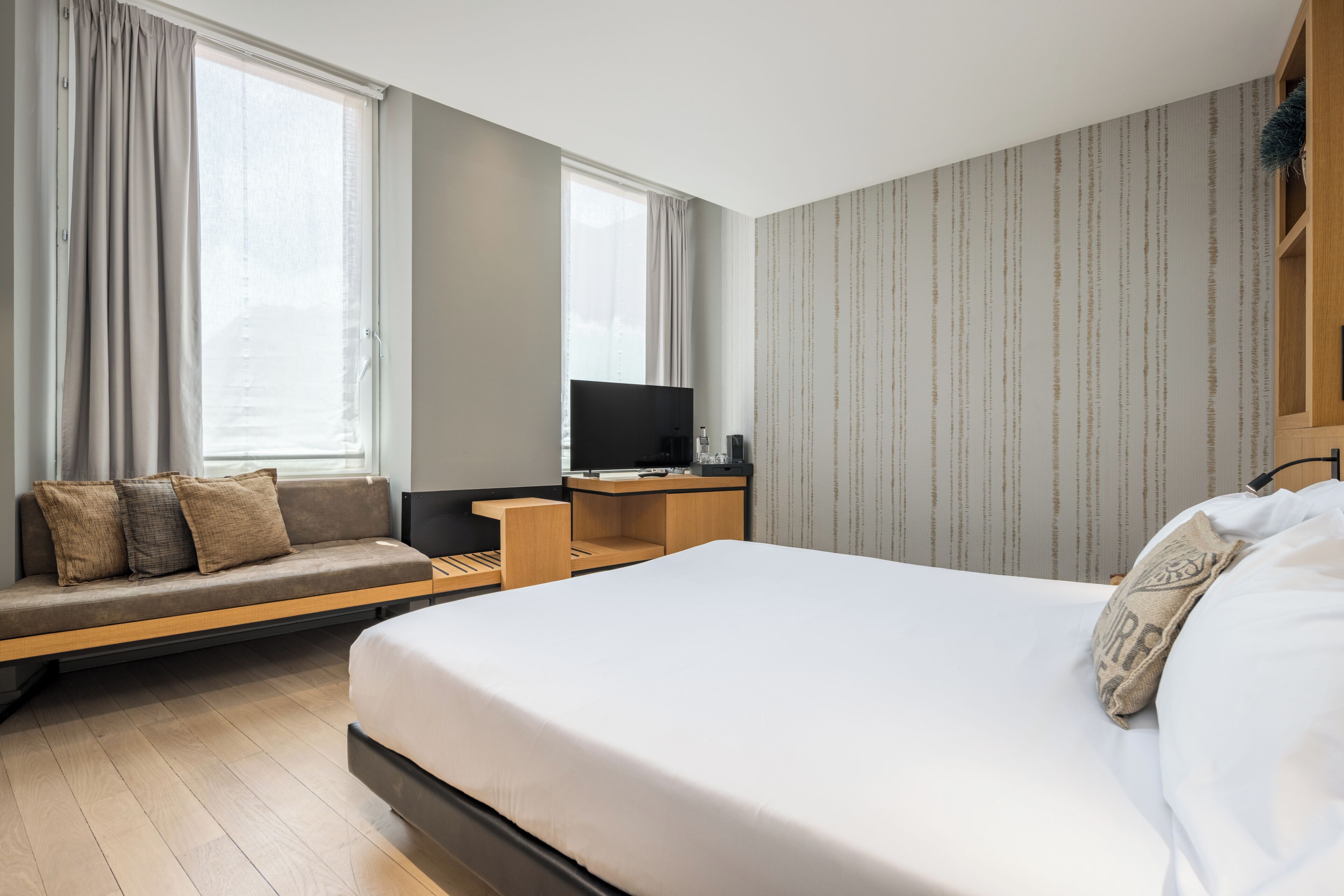 A modern hotel room with a large bed, a sofa, a desk, and a TV.