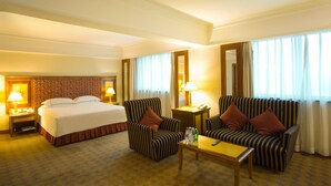 Une chambre d’hôtel avec un grand lit, deux fauteuils, une petite table et une table de chevet avec des lampes.