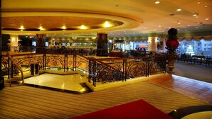 Un hall d’entrée spacieux, agrémenté d’un grand escalier, d’une colonne centrale et d’un espace détente avec des tables et des chaises.