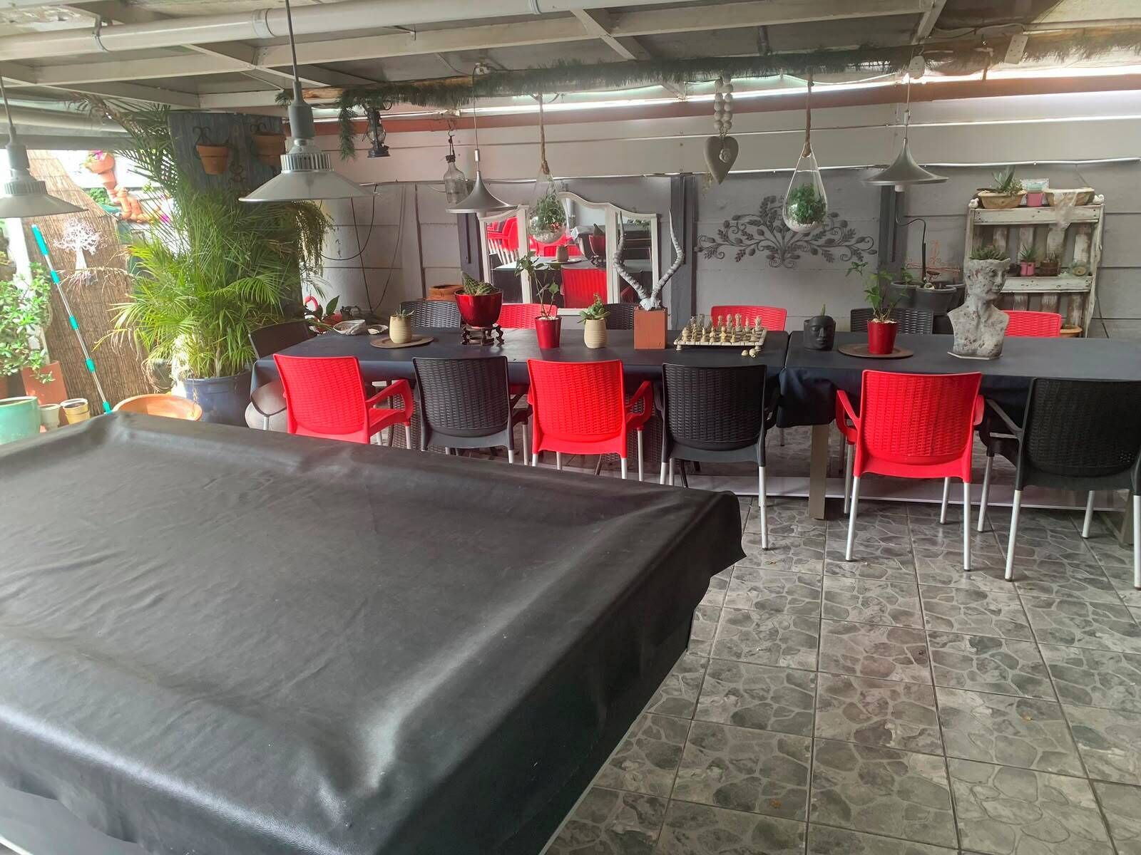 Ein Restaurant mit Terrassensitzgelegenheiten, Tischen mit roten Stühlen, hängenden Pflanzen und einem Schachbrett auf einem Tisch.