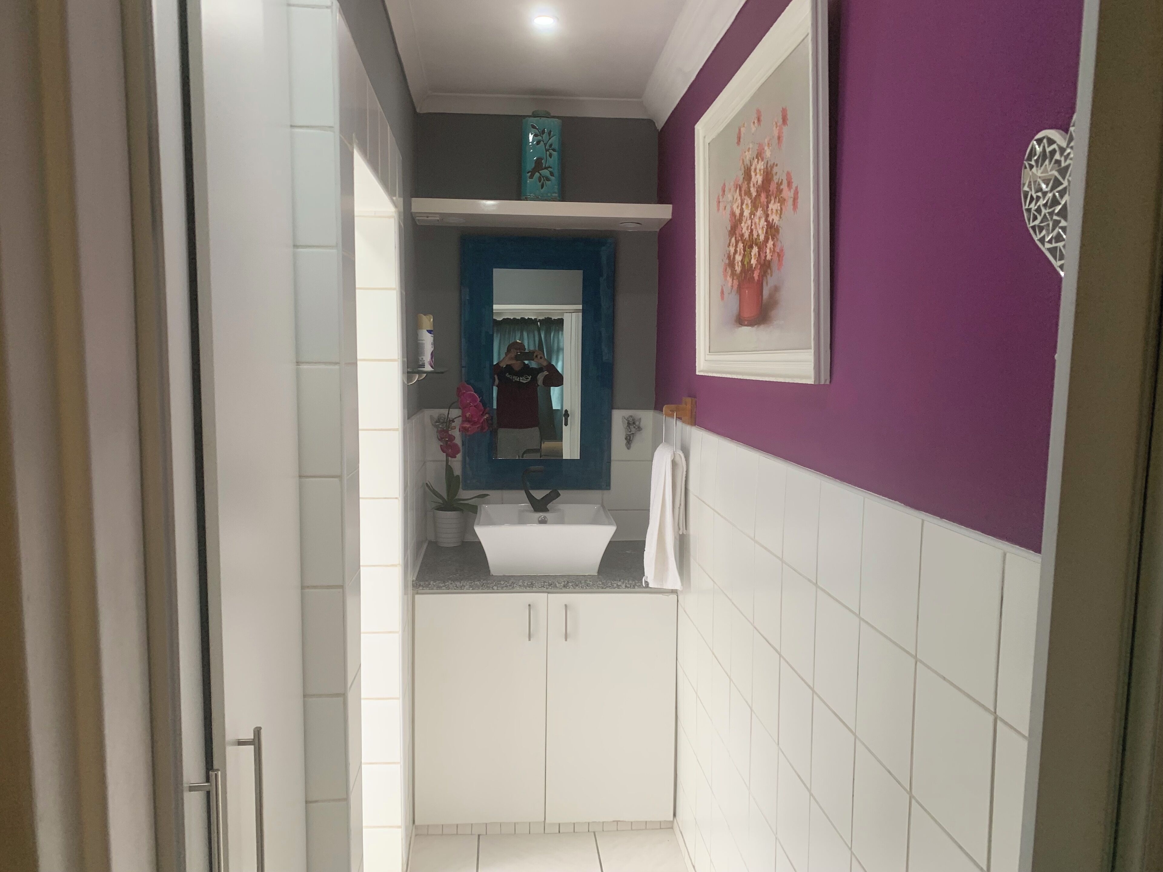 A narrow bathroom with white tiles, a sink, a mirror, and a purple wall.