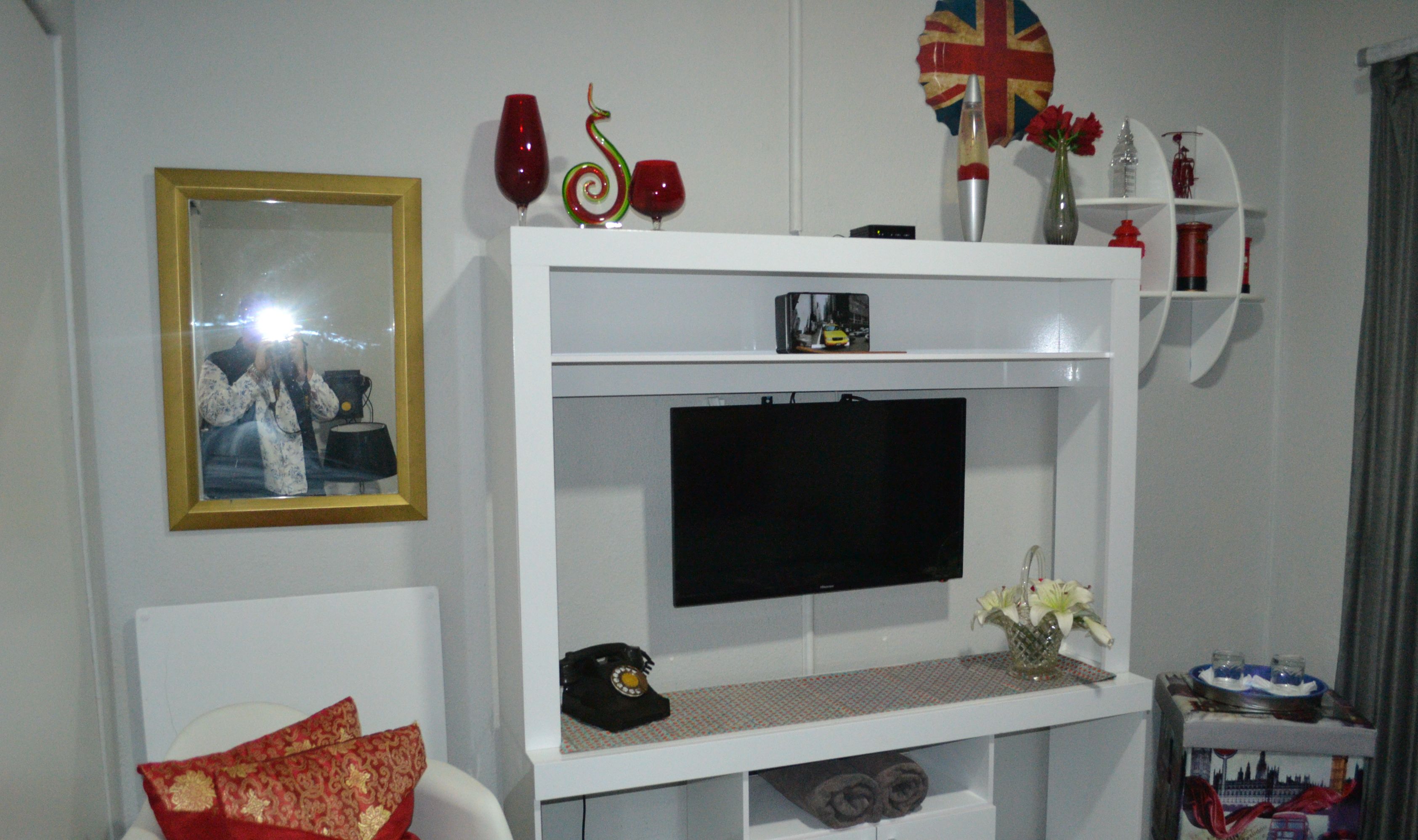 Een woonkamer met een wandtelevisie, een lijst met een afbeelding en een plank met decoratieve objecten.