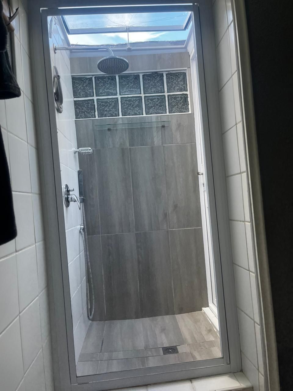 Area doccia vetrata con lucernario, pareti in piastrelle e porta in legno.