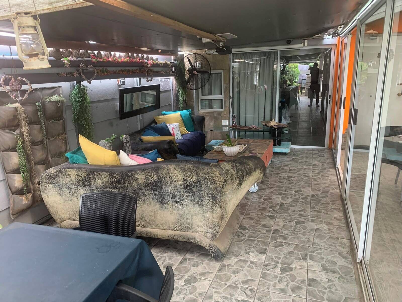 Ein Sitzbereich im Freien mit einer Couch, Kissen, einem Ventilator und einem Fernseher.