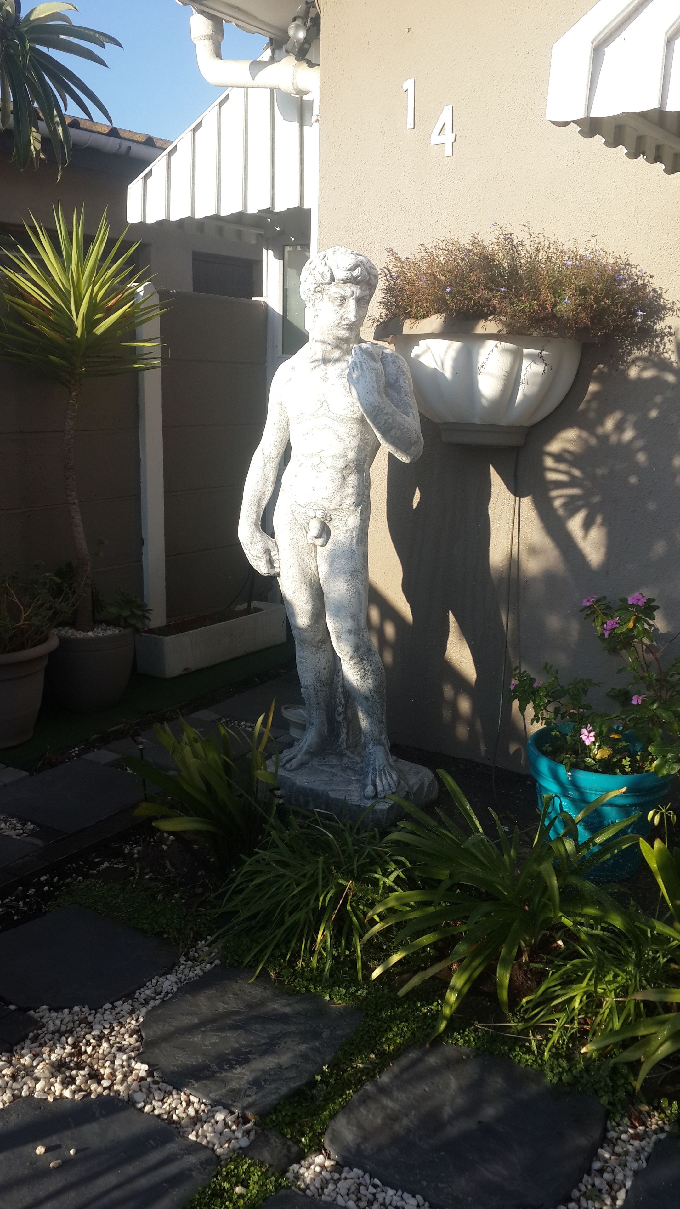 Eine Statue in einem Garten mit Blumentöpfen und der Gebäudenummer 14 im Hintergrund.