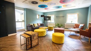 A modern lounge area with a sofa, ottomans, and a coffee table. - Jonas Hotel (Sheffield)