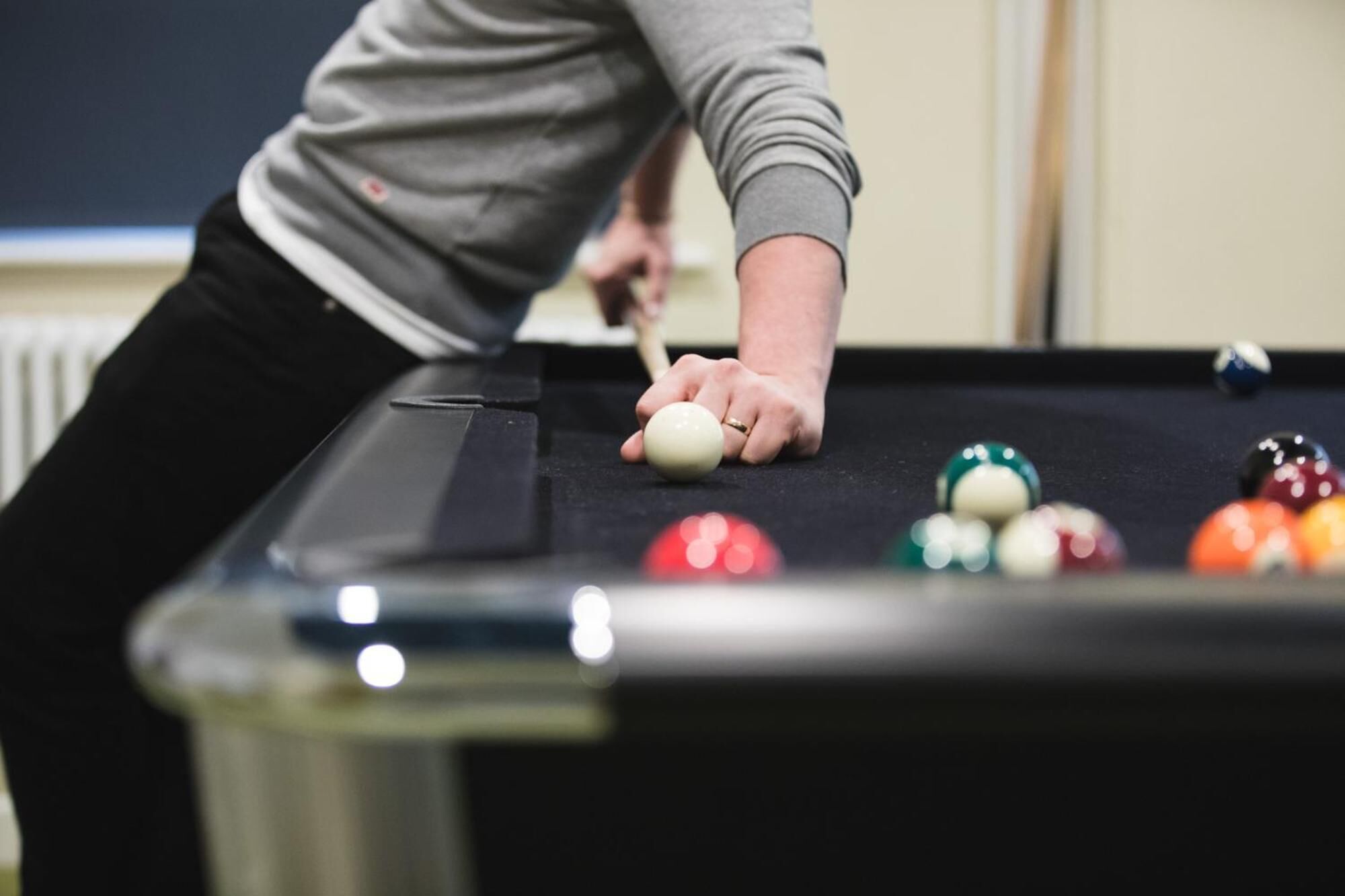 A person playing pool, focusing on the cue stick and balls on the table.