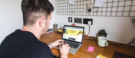 A person working at a wooden desk with a laptop, a mug, and a small plant.