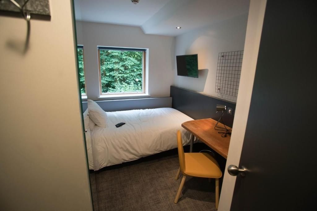 Un dormitorio con cama, escritorio, silla, ventana y puerta.