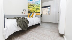 A bedroom with a bed, a window, and a wall-mounted lamp. - Jonas Hotel (Sheffield)