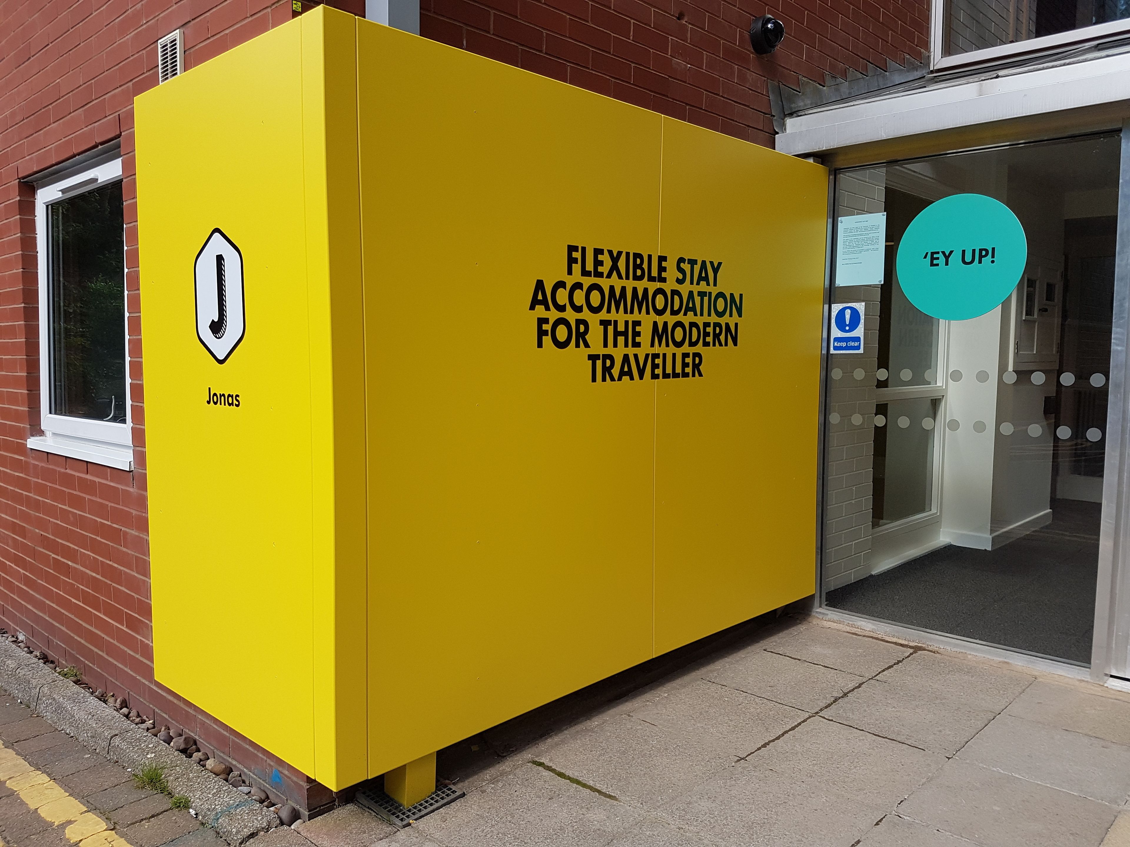 Ein gelbes Unterkunftsmodul mit einem Schild, auf dem steht: 'Flexible Stay Accommodation for the Modern Traveller.'