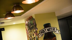 A ceiling with three pendant lights and a wall with a colorful mural and a bottle labeled "HOLY WATER." - Jonas Hotel (Sheffield)