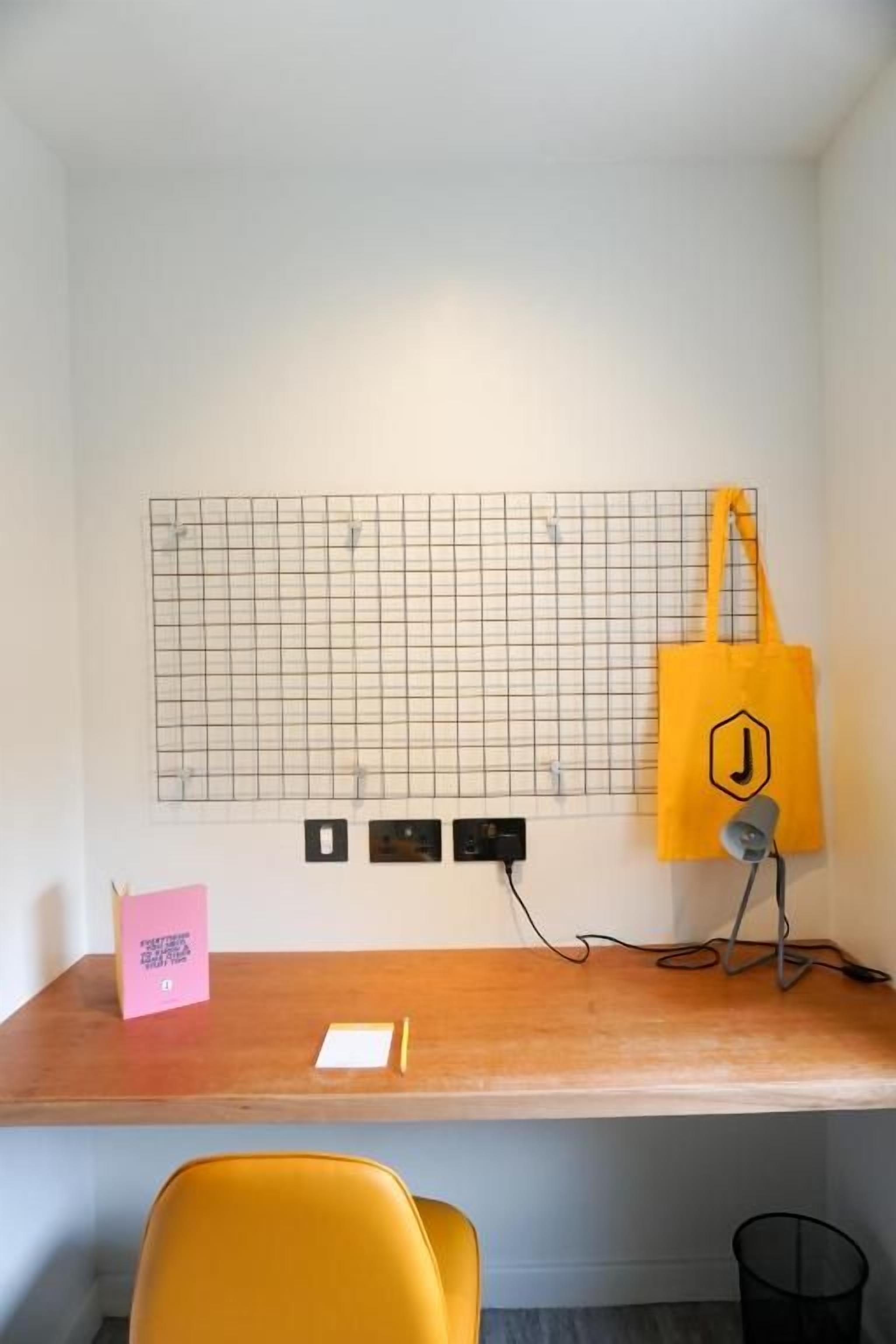 Un espacio de trabajo con un escritorio de madera, una silla amarilla, un tapiz de diseño de cuadrícula y una bolsa de tela amarilla.