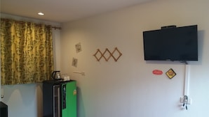 A room with a flat-screen TV mounted on the wall, a refrigerator, a coffee maker, and a patterned curtain. - Paaon Resort Khaoyai (Pak Chong)