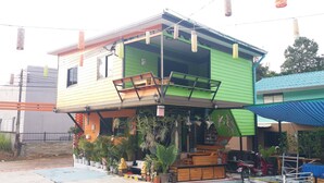 A two-story house with a green and yellow exterior, a balcony, and various potted plants. - Paaon Resort Khaoyai (Pak Chong)
