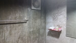 A bathroom with a toilet, a towel rack, a shelf with toiletries, and a wall-mounted fan. - Paaon Resort Khaoyai (Pak Chong)