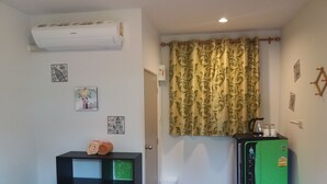 A compact room with a bed, a small black storage unit with green panels, a green refrigerator, and a wall-mounted air conditioner. - Paaon Resort Khaoyai (Pak Chong)