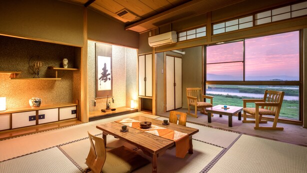 A traditional Japanese room with tatami flooring, a low wooden table, and chairs. There is a large window with a view of the sea. - Yumoto Kobayashi (Kurume)