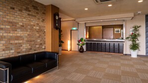 A reception area with a brick wall, a wooden panel, a black leather sofa, a reception desk, and a potted plant. - Yumoto Kobayashi (Kurume)