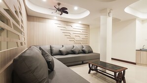 Un salon moderne avec un canapé d’angle, une table basse en verre, un éclairage encastré au plafond et un panneau mural en bois intégré.