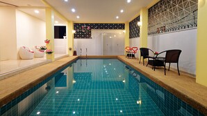Une piscine dont les murs et le sol sont recouverts de carreaux, entourée de chaises et d’une petite table.