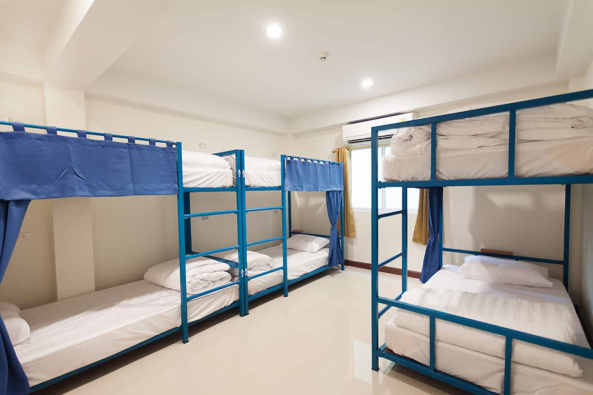 Ett rum med våningssängar placerade i en rad, alla med en blå ram och vita sängkläder.