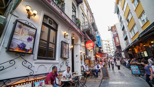 Une rue animée où l’on trouve un restaurant appelé « Sarnic » et qui dispose de tables en terrasse.