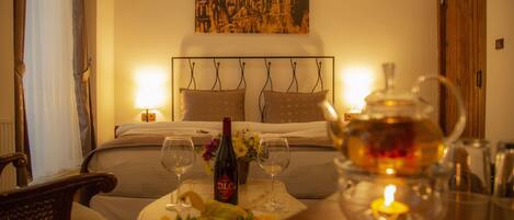 A hotel room with a bed, a bedside table with a bottle of wine, glasses, and a candle.