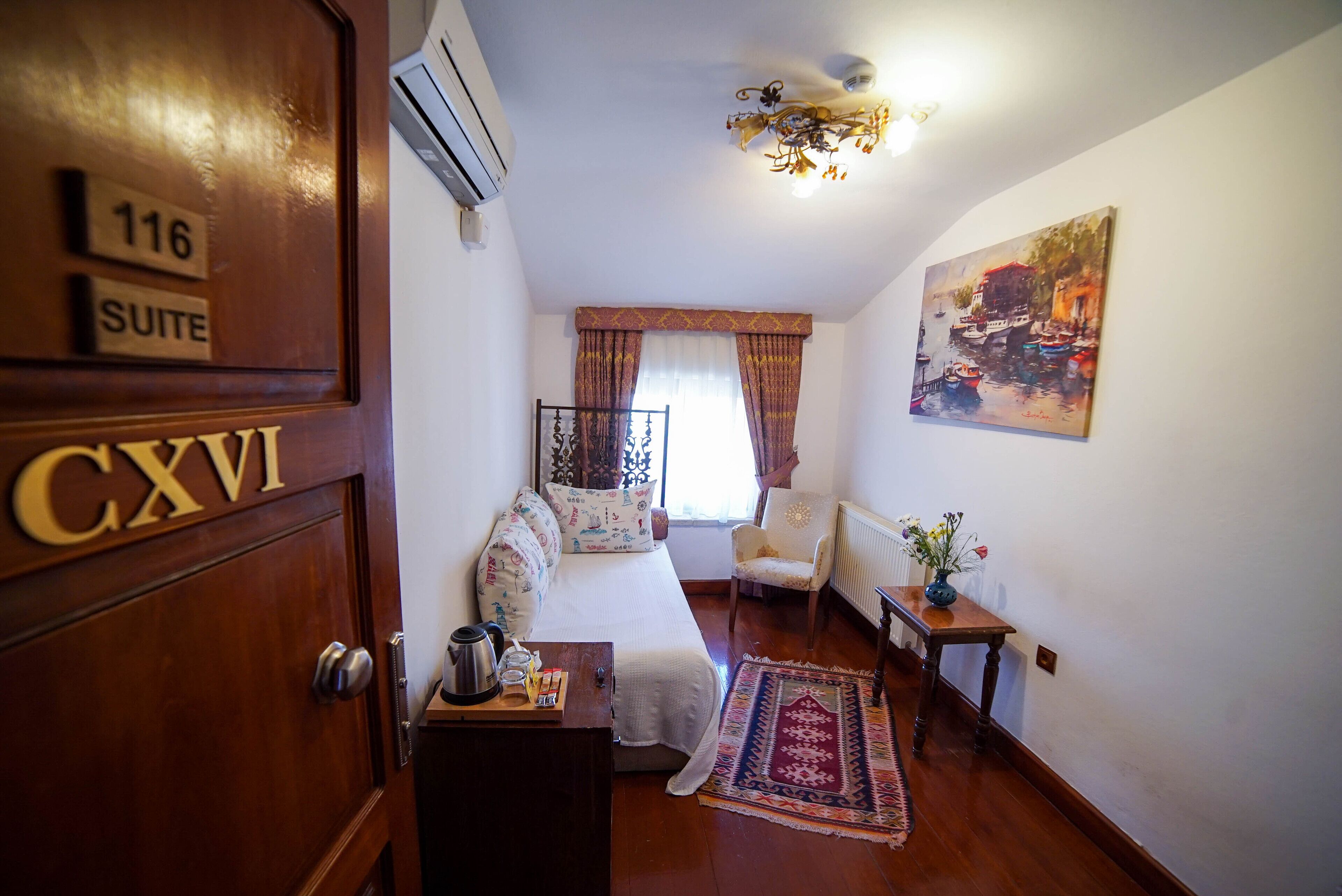 A hotel room with a bed, a chair, a small table with a vase, and a painting on the wall.