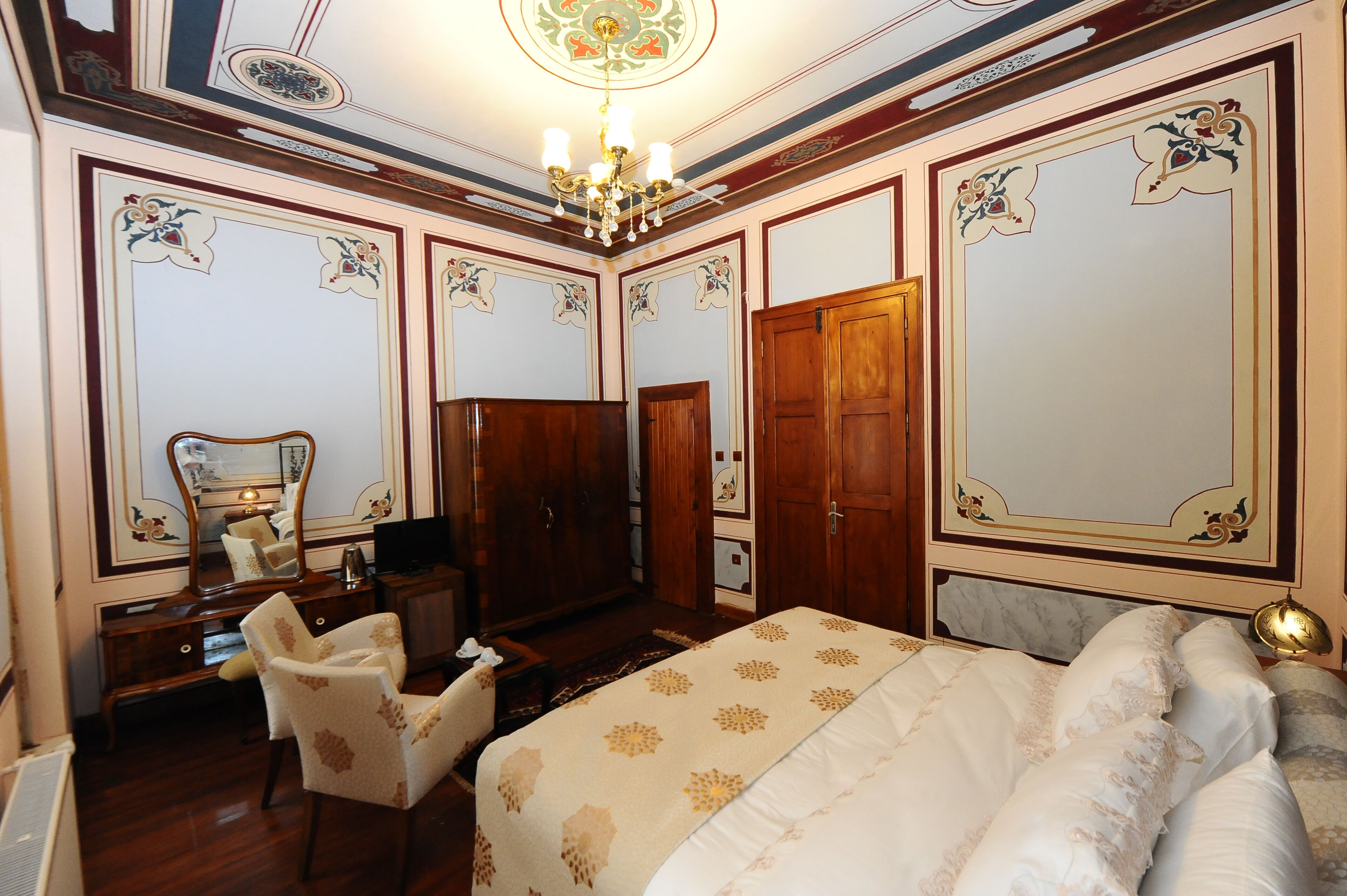Un dormitorio con una cama grande, un armario de madera, un escritorio con silla y un espejo.