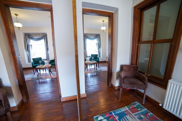 A room with wooden flooring, a green armchair, a small table with a glass, and a window with curtains. - Sarnic Butik Hotel (Istanbul)