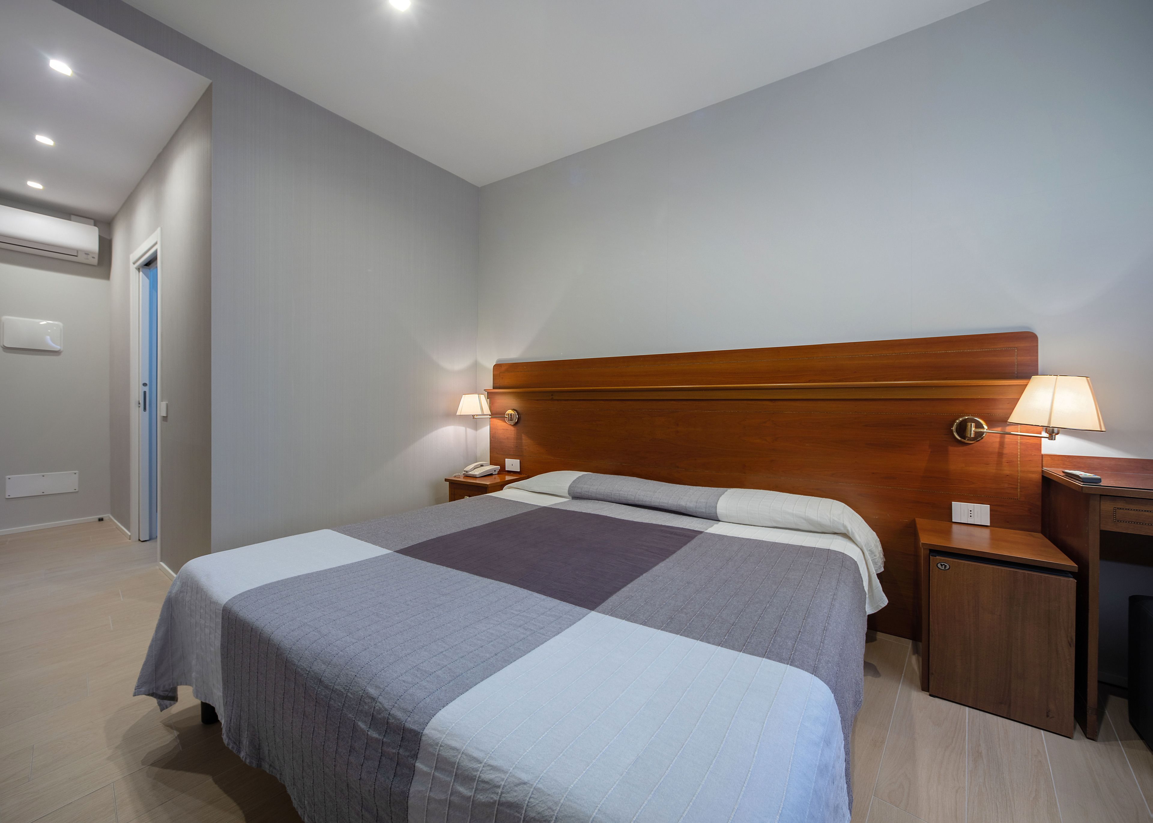 A neatly made bed with a checkered bedspread, two bedside lamps, a wooden headboard, and a nightstand with a phone.