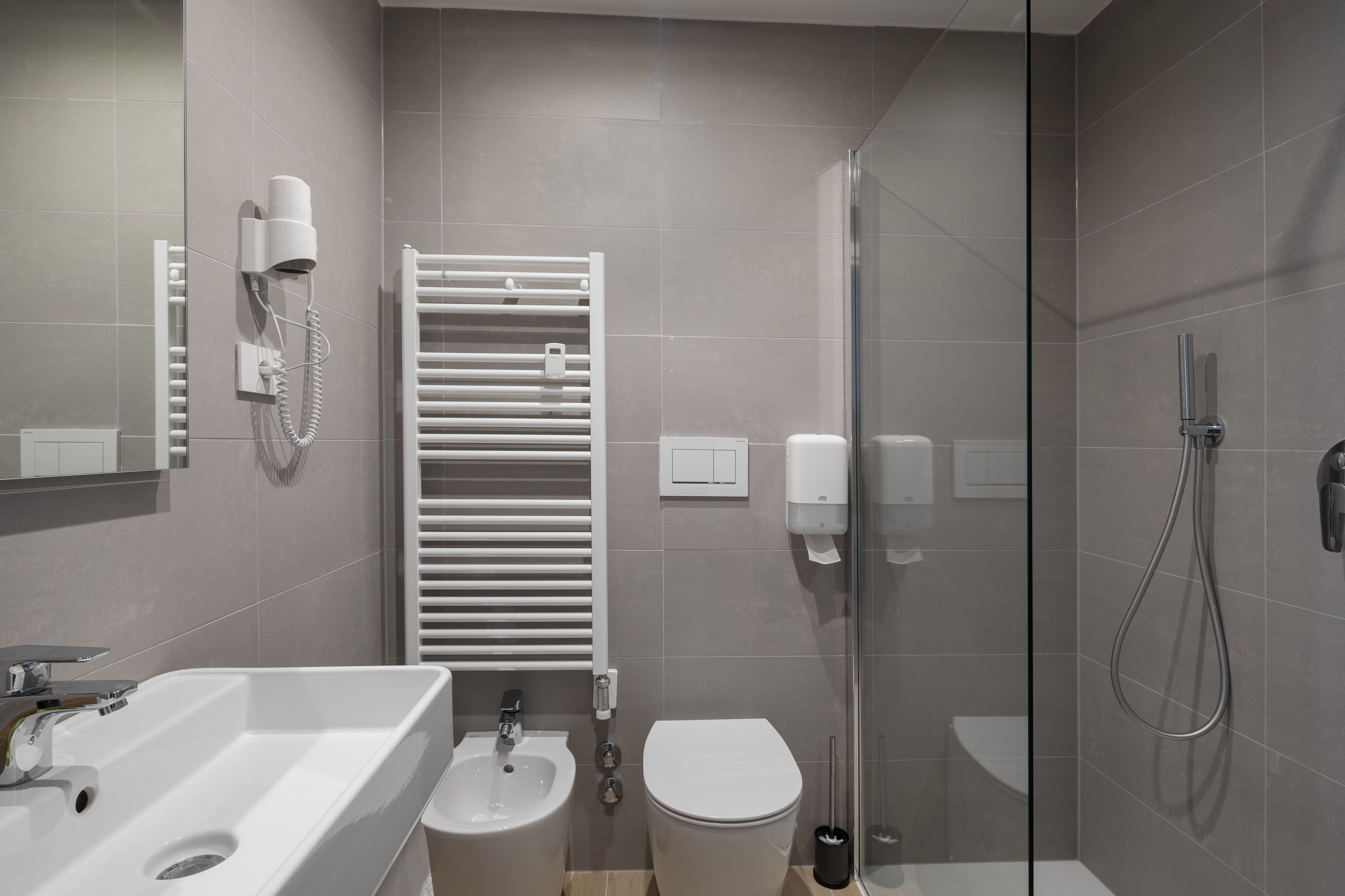 Ein modernes Badezimmer mit Waschbecken, Bidet, Toilette, Handtuchhalter und einer Duschkabine.
