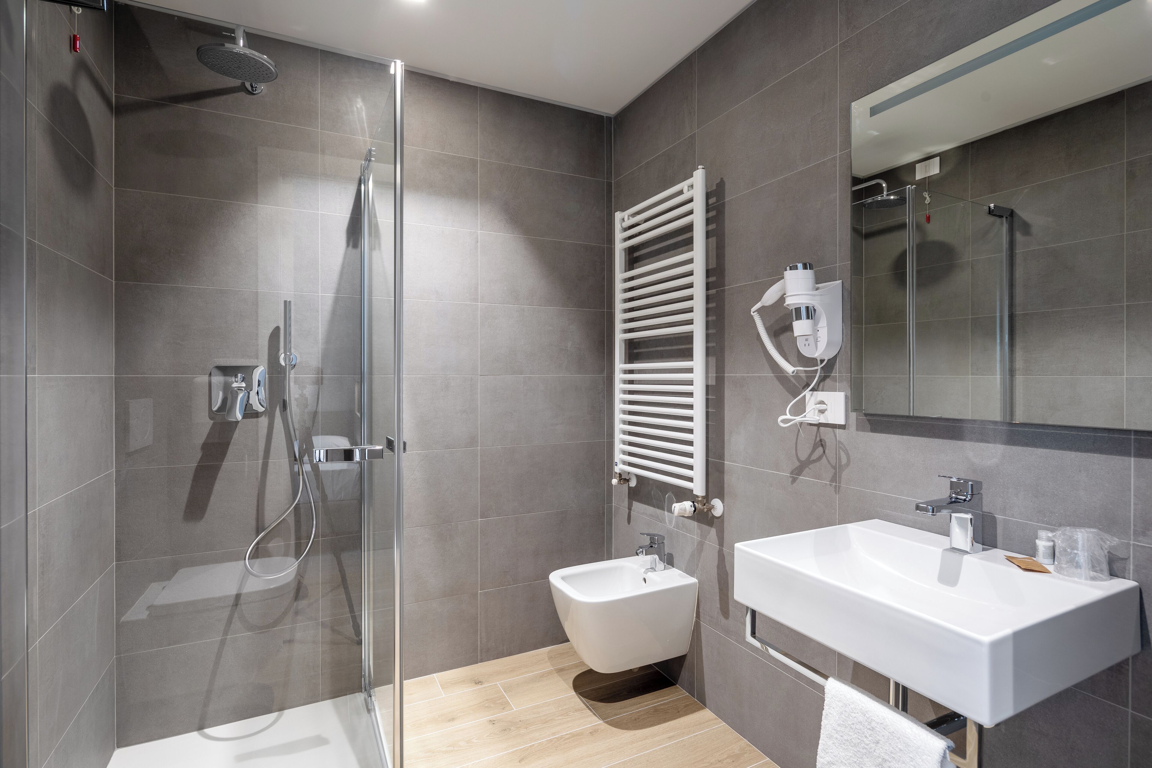 Un baño moderno con ducha de vidrio, un bidé y un lavamanos blanco.