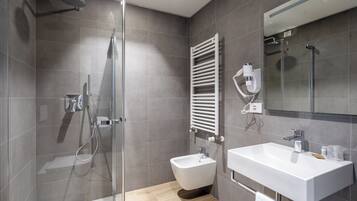 Un baño moderno con ducha de vidrio, un bidé y un lavamanos blanco.