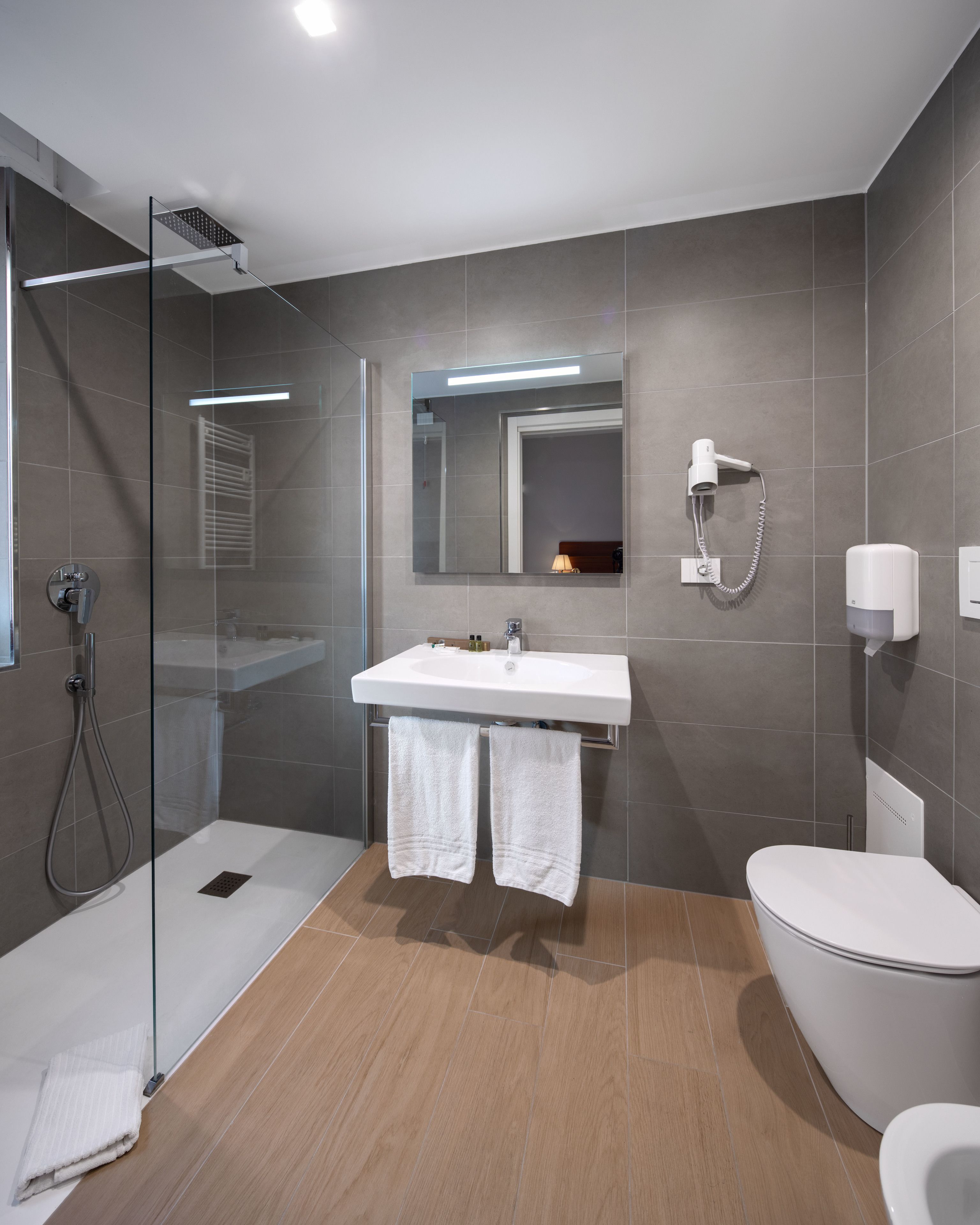 A modern bathroom with a glass-enclosed shower, a white sink with a mirror above, and a toilet.
