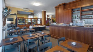 A restaurant with multiple tables and chairs, a bar area with a counter, and a display case with food items. - Hotel Excelsior (Pavia)