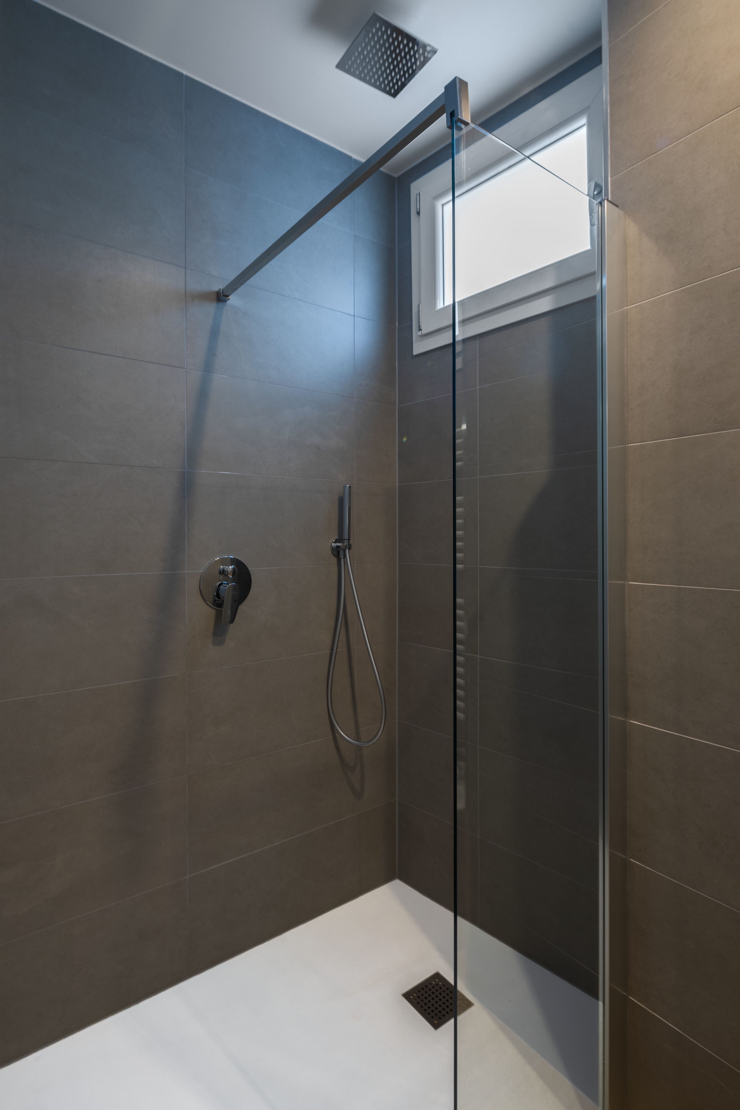 Een moderne douche met een glazen deur, een handdouche en een bedieningspaneel.