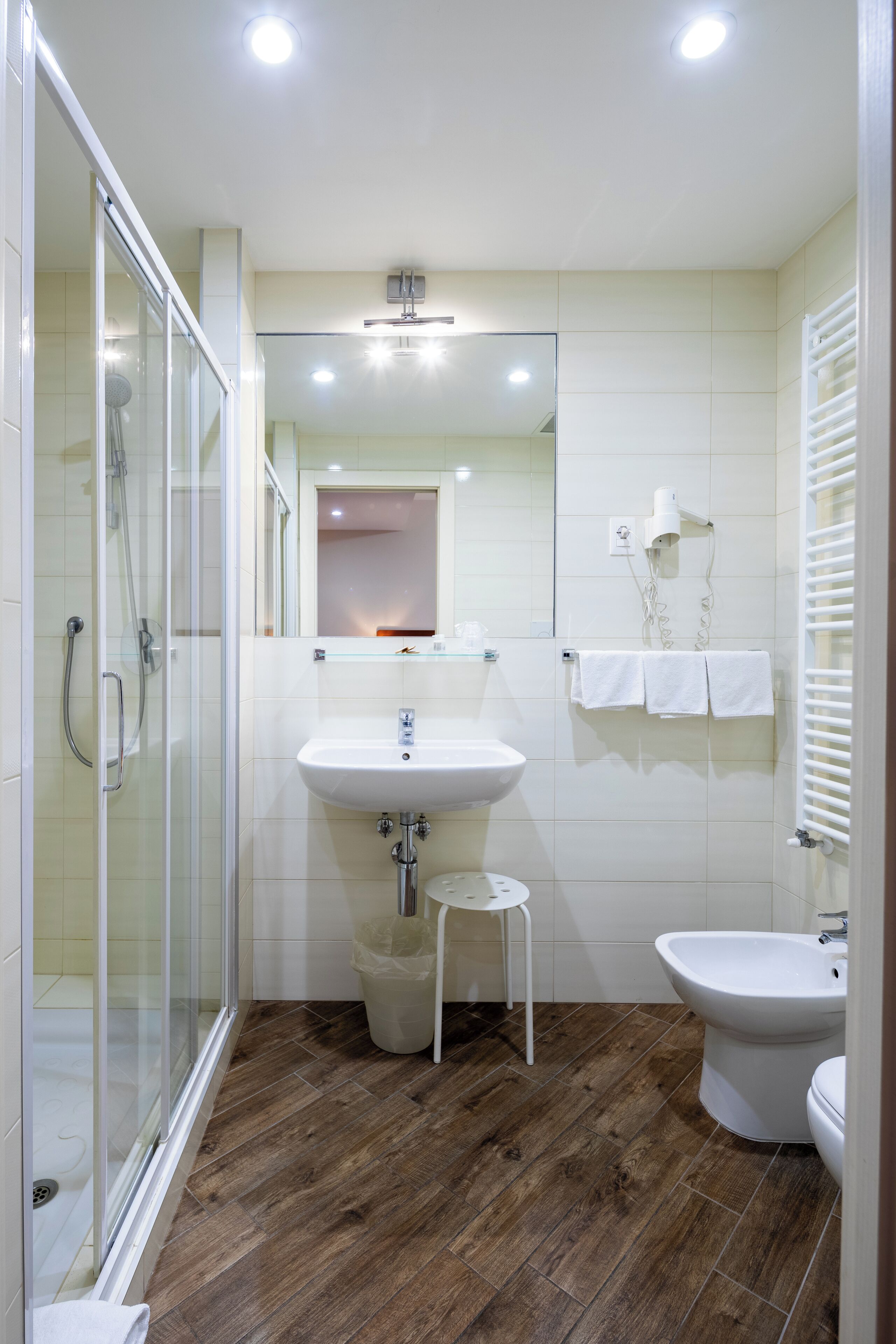 Un bagno moderno con box doccia in vetro, lavabo su piedistallo, bidet e specchio sopra il lavabo.