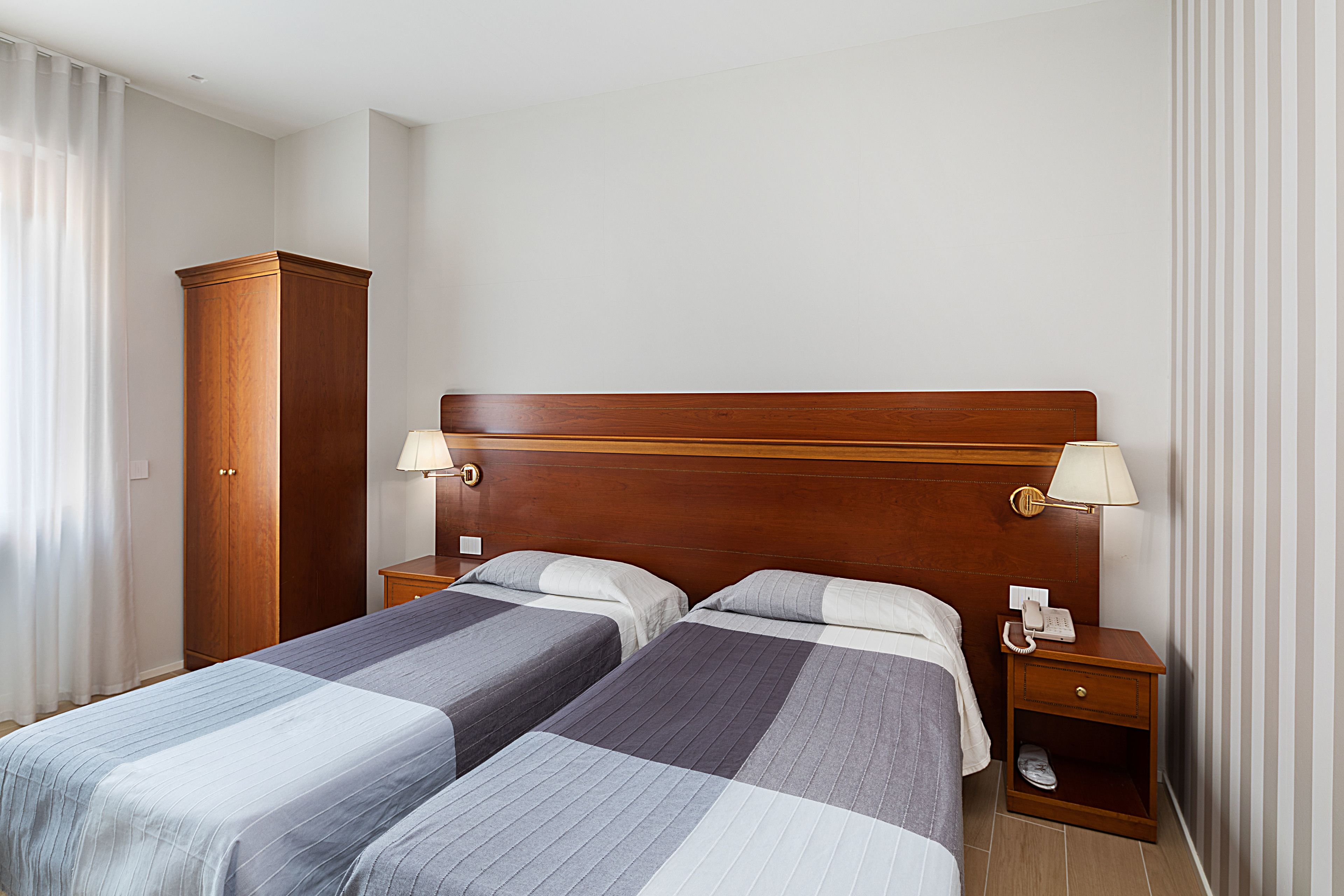 Habitación de hotel con dos camas, cabecero de madera, lámparas de noche, teléfono y armario.