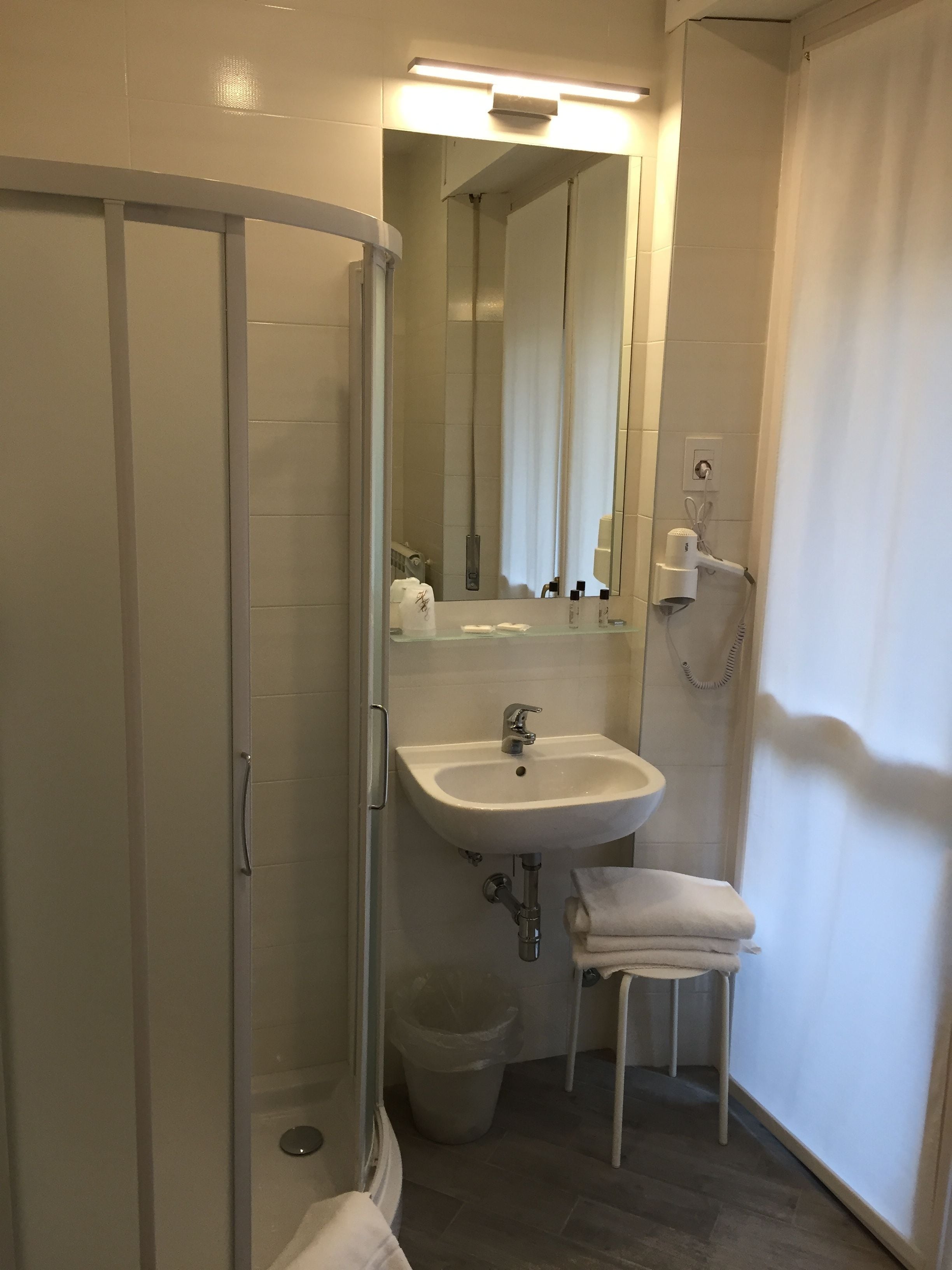 Een moderne badkamer met een douchecabine van glas, een witte wastafel en een klein handdoekrek.