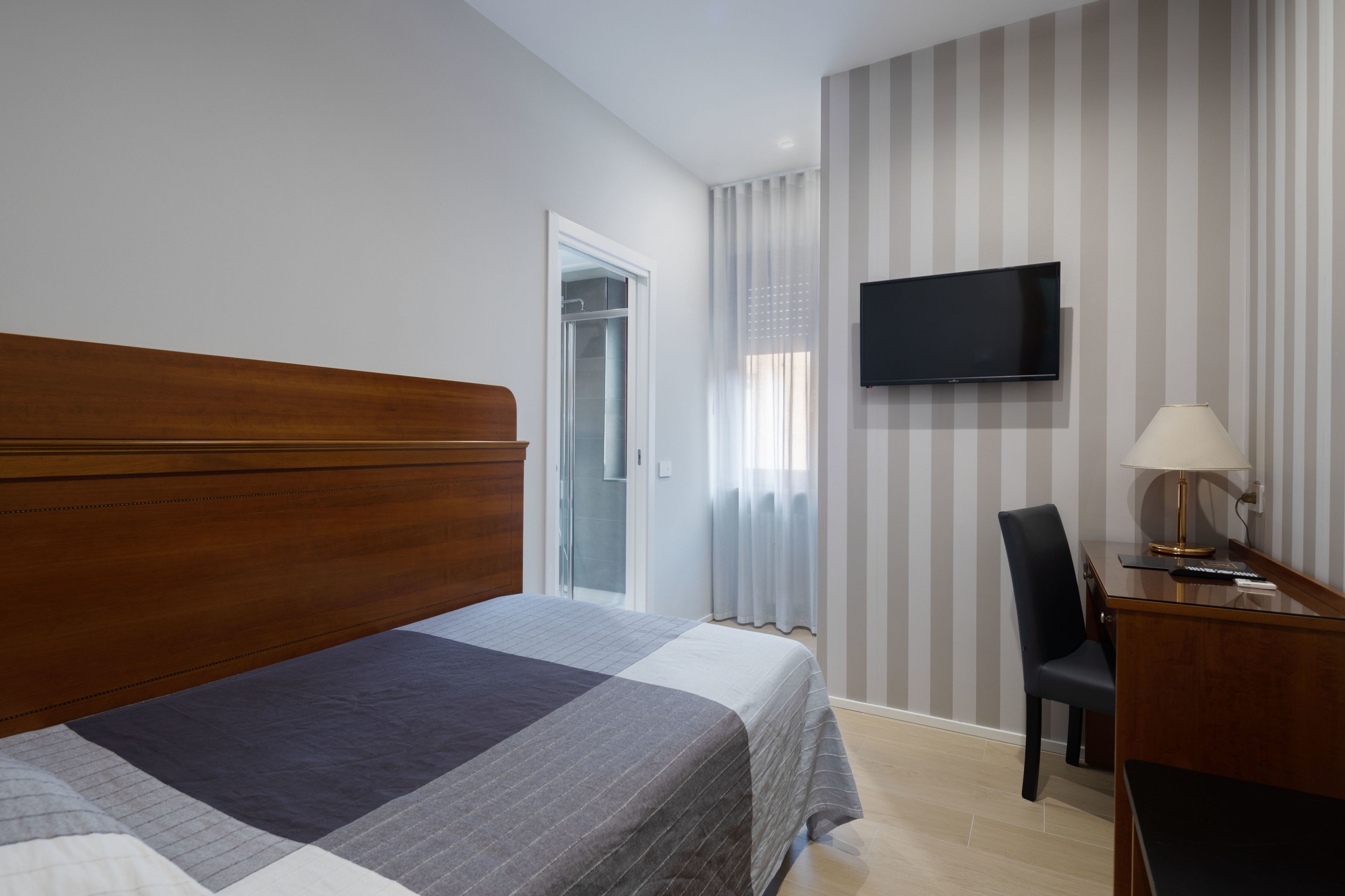 Habitació d'hotel amb un llit gran, una taula de treball amb una làmpada, una televisió i una porta corredissa al bany.