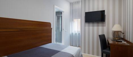 Una habitación de hotel con una cama grande, un escritorio con lámpara, televisión y una puerta corredera al baño.