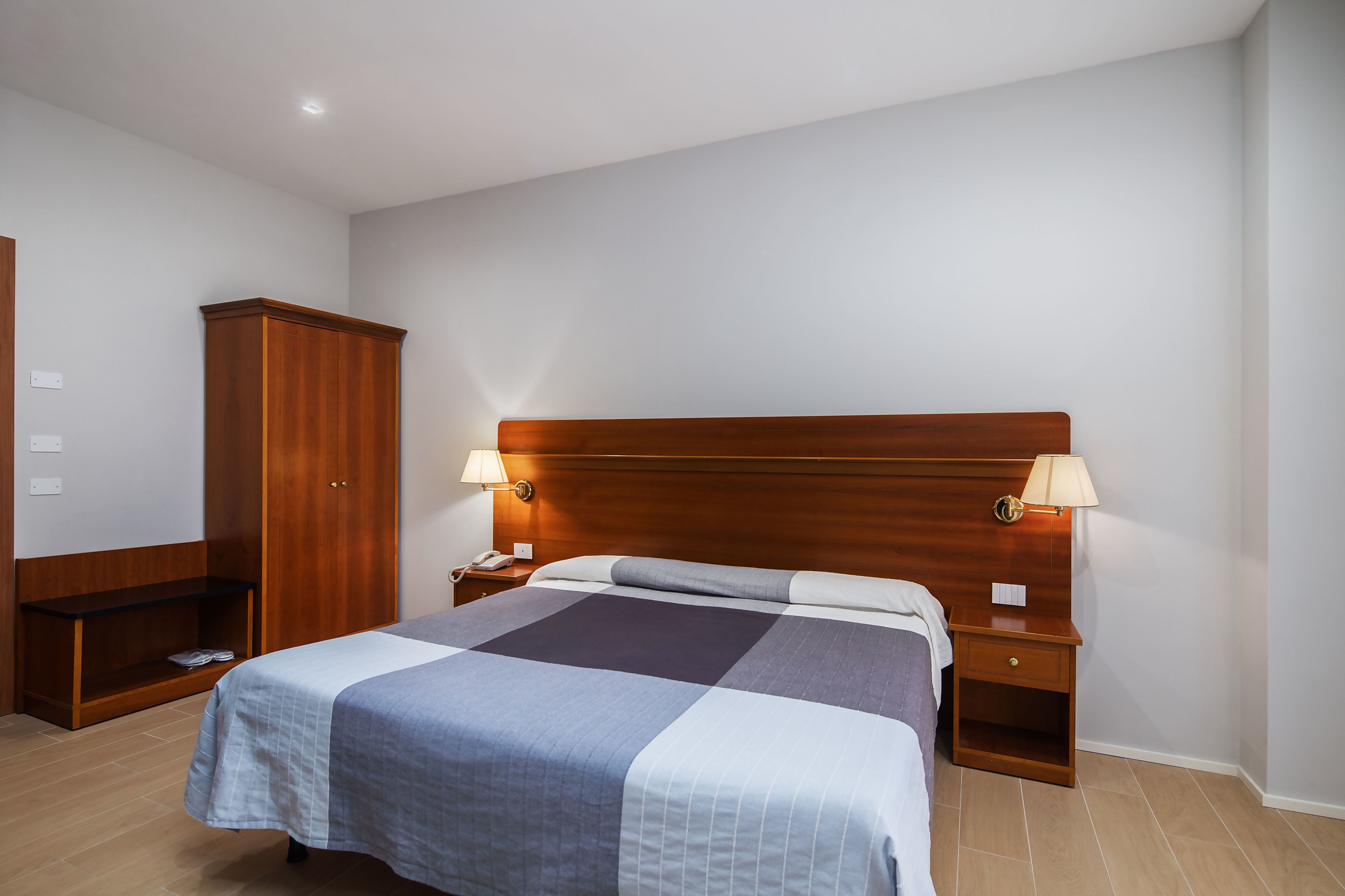 Een keurig ingerichte hotelkamer met een groot bed, een houten hoofdbord, bedlampjes, een kledingkast en een klein plankje.