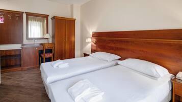 A hotel room with two beds, a wooden headboard, a nightstand, a desk, and a wardrobe.