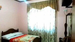 Un dormitorio con cama, cortinas, televisión y una silla.