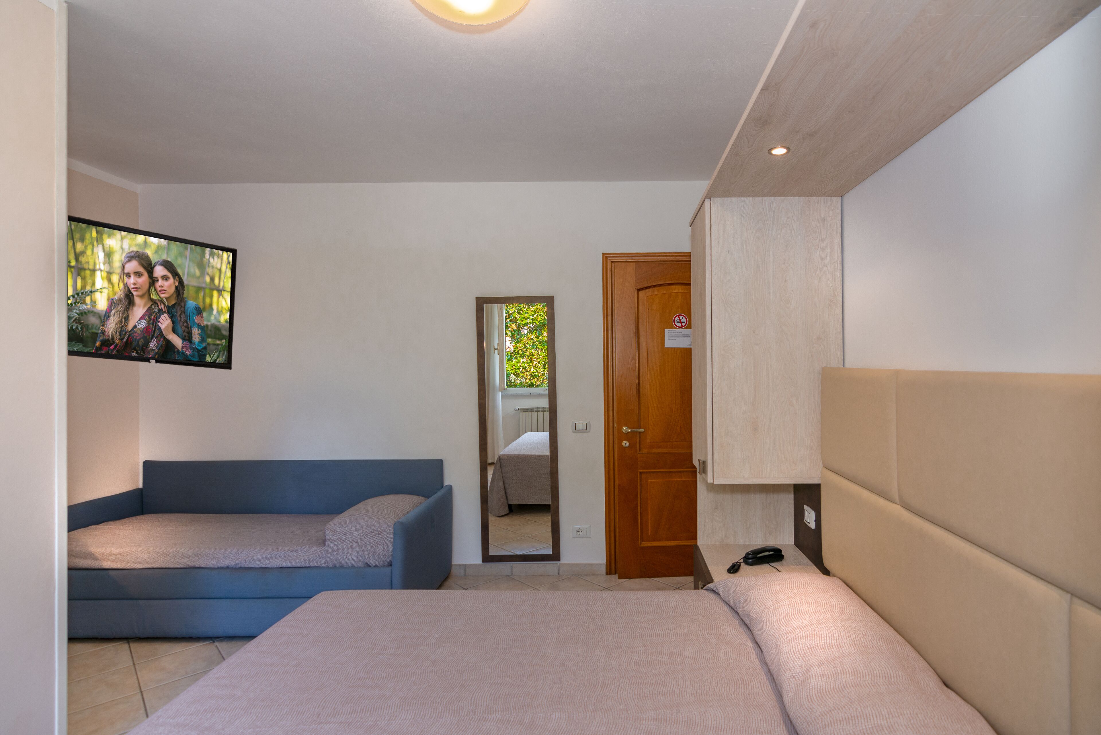 Ein Schlafzimmer mit einem Bett, einem blauen Sofa, einem Holzschrank und einem Fernseher an der Wand.